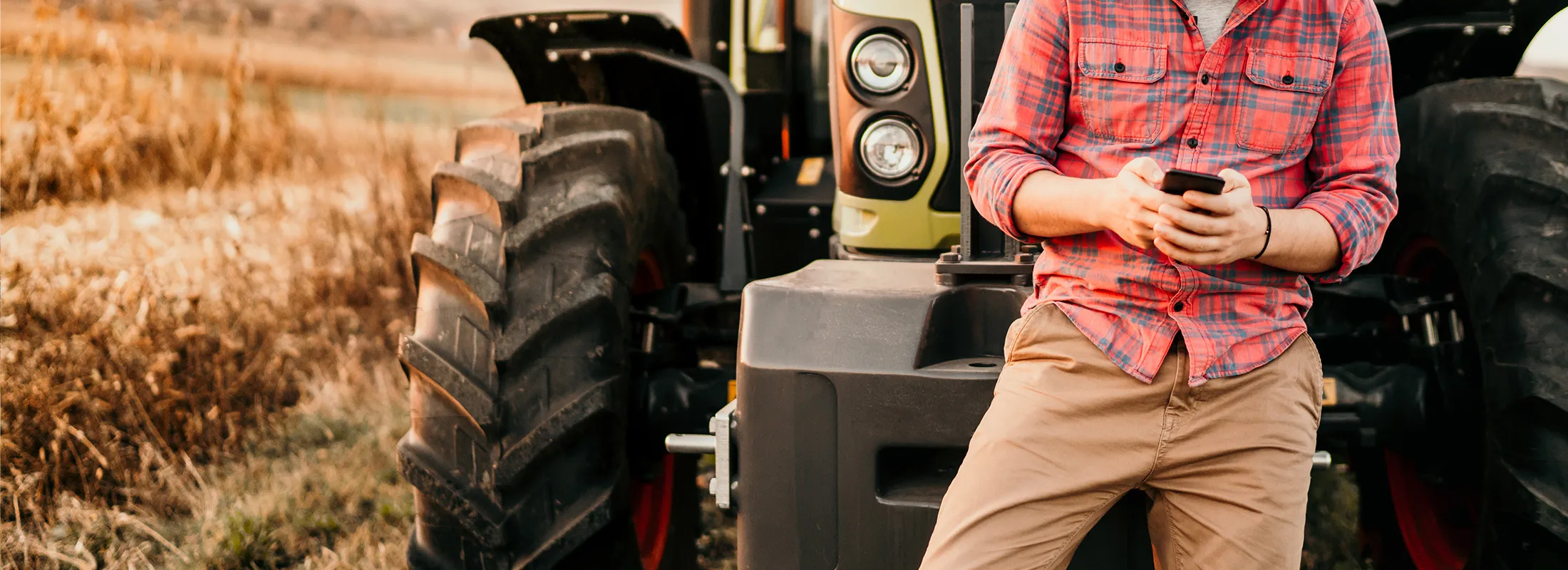 a person on their phone leaning on a tractor in a field