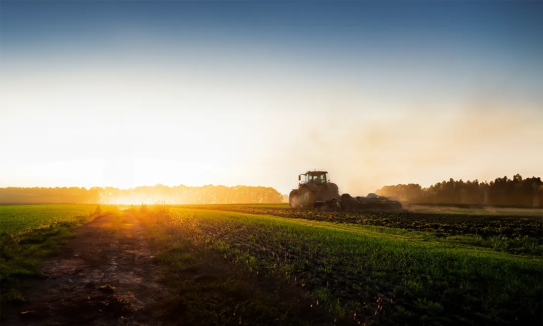 Tractor driving away in the distance at sunset
